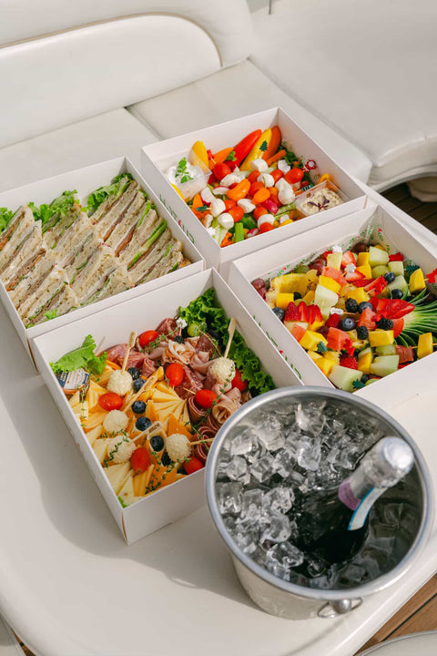 Assorted food items including sandwiches and salads in a compartmentalized container with a bucket of ice.
